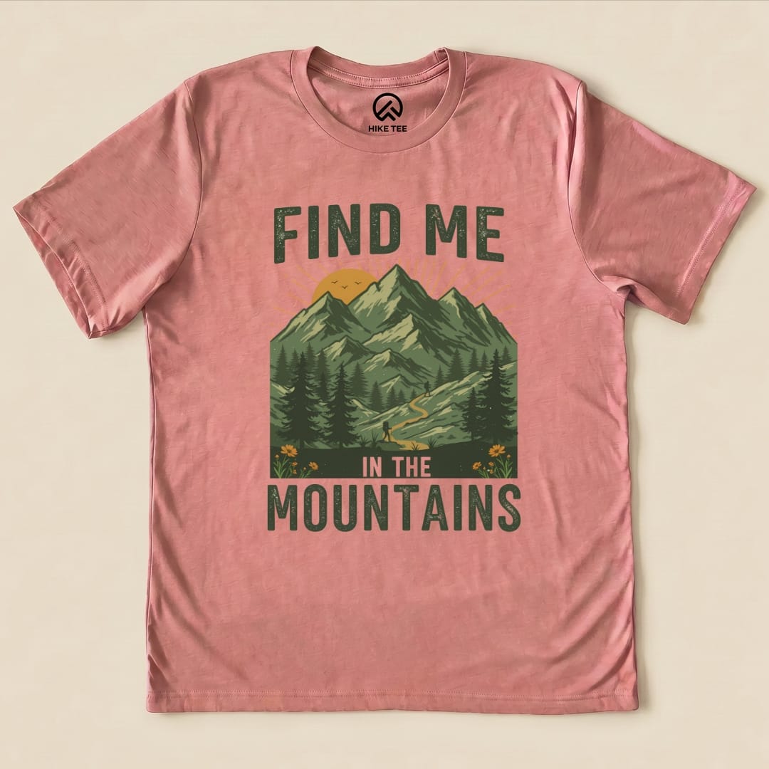 A pink graphic t-shirt features the phrase "Find Me In The Mountains" with a mountainous landscape and hiking trail design.