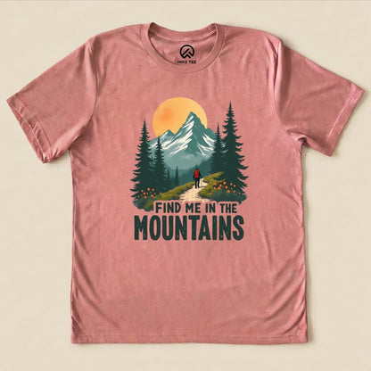 A pink graphic t-shirt featuring a mountain scene and the slogan "FIND ME IN THE MOUNTAINS" above a hiker on a trail.