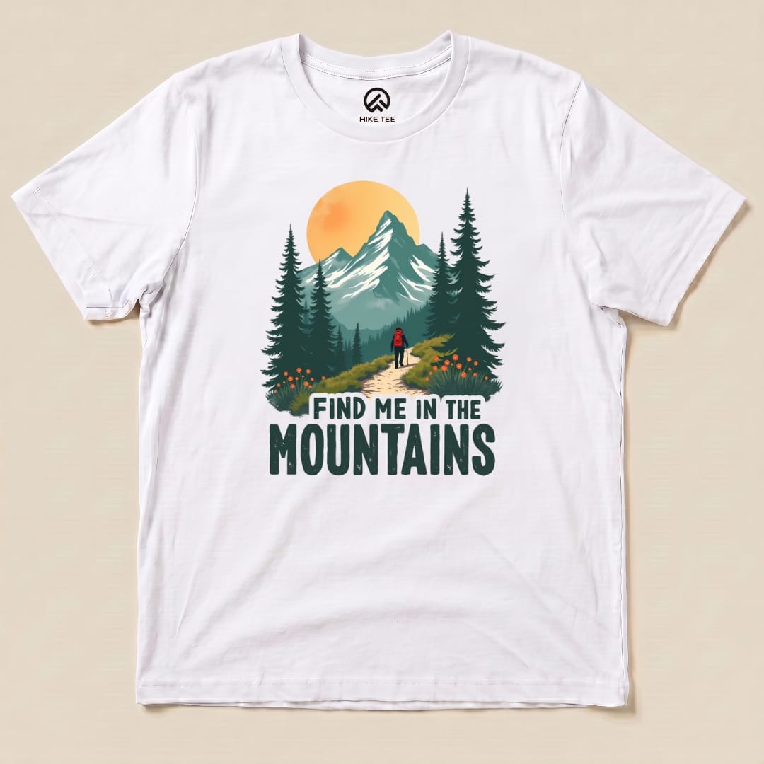 A graphic t-shirt featuring a hiker on a forest path with mountains and the phrase "Find Me In The Mountains.