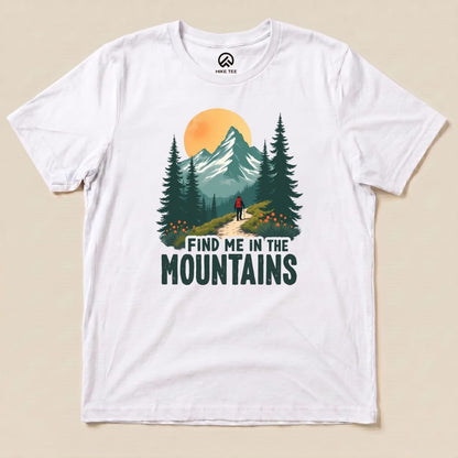 A graphic t-shirt featuring a hiker on a forest path with mountains and the phrase "Find Me In The Mountains.