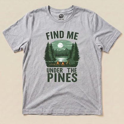 A gray graphic t-shirt features a serene camp scene with the words "Find Me Under The Pines" above a lake and mountains.