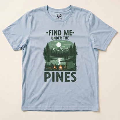 A light blue graphic t-shirt featuring the phrase "Find Me Under The Pines" along with a scenic illustration of a campsite, trees, and mountains.