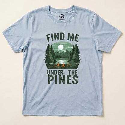 A light blue graphic t-shirt featuring a campfire scene with trees and mountains, reading "Find Me Under The Pines Shirt.