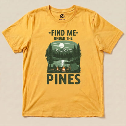 A yellow graphic t-shirt featuring the phrase "Find Me Under The Pines" with a scenic camping illustration, including trees and mountains.