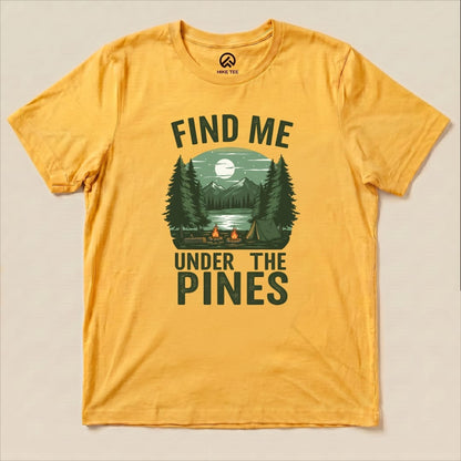 Graphic t-shirt featuring the phrase "Find Me Under The Pines" with a serene forest scene, mountains, and a campfire design.