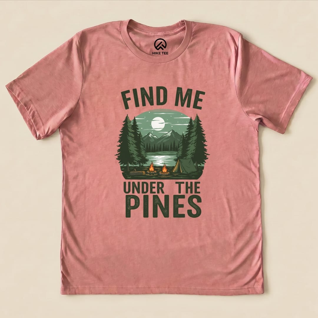 The graphic t-shirt features the phrase "Find Me Under The Pines" alongside a scenic design of trees, mountains, and a campfire.