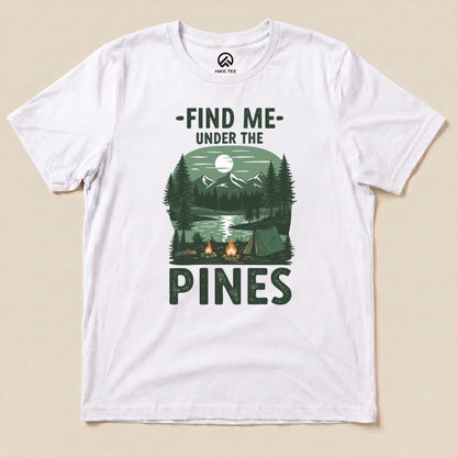 Graphic t-shirt featuring a serene forest landscape with the slogan "Find Me Under The Pines" and imagery of mountains, trees, and a lake.