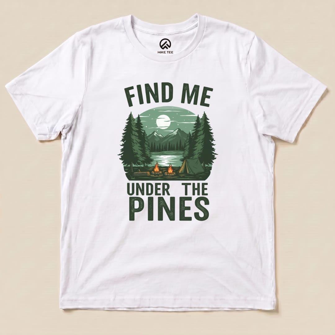 A white graphic t-shirt features the slogan "Find Me Under The Pines" with a scenic design of trees, mountains, and a lake.