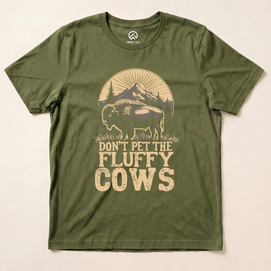 A graphic t-shirt in olive green featuring a fluffy bison with the text "DON'T PET THE FLUFFY COWS" beneath it.