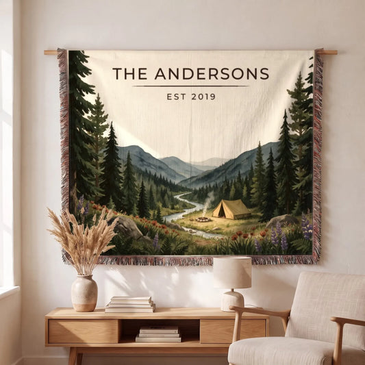 A beautifully illustrated "Forest Campsite Woven Blanket" featuring a serene camping scene with mountains, forest, and a tent.