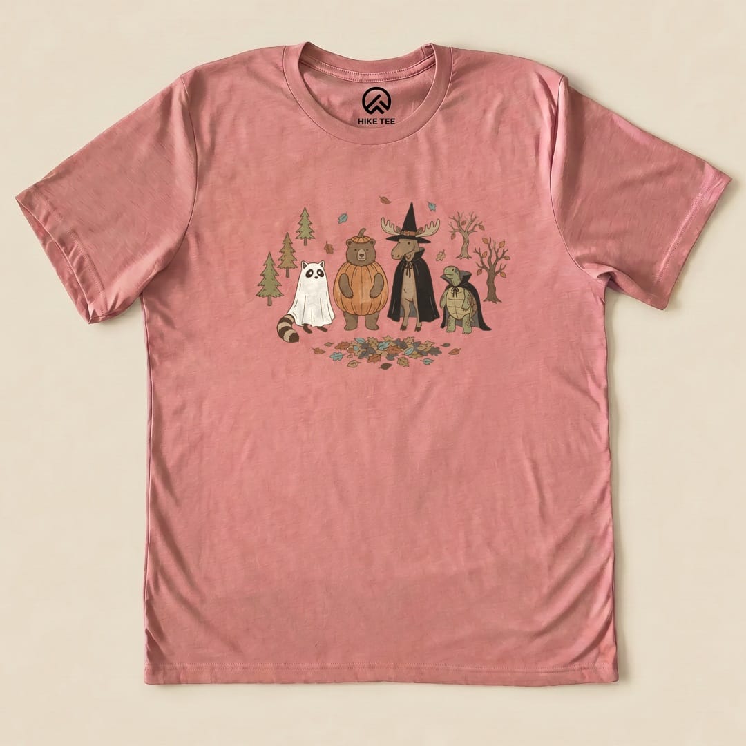 A pink graphic t-shirt featuring a whimsical design of forest animals in costumes, titled "Forest Friends Costume Party Shirt.