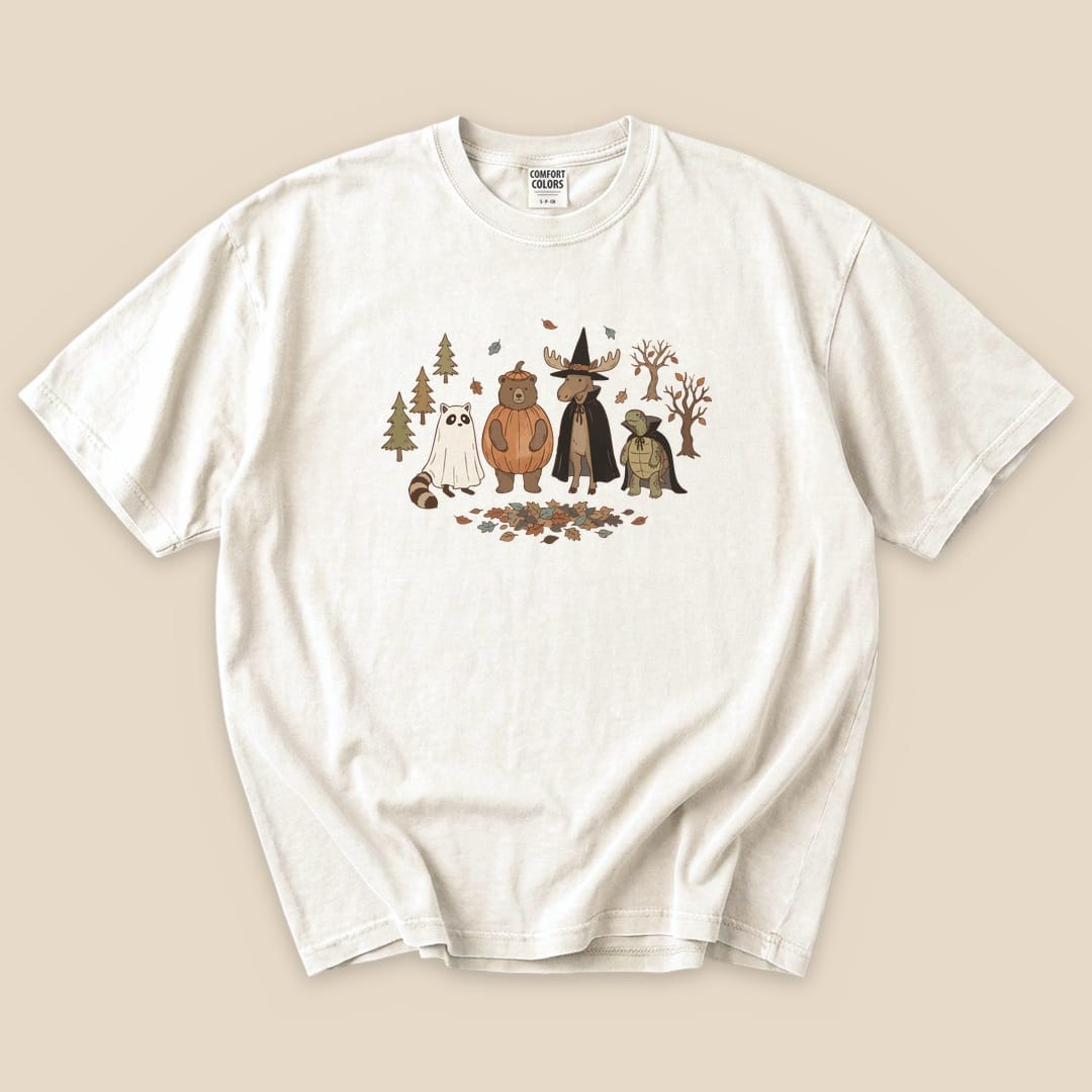 The Forest Friends Costume Party T-Shirt features a playful graphic of a bear, moose, raccoon, and ghost among trees and autumn leaves.