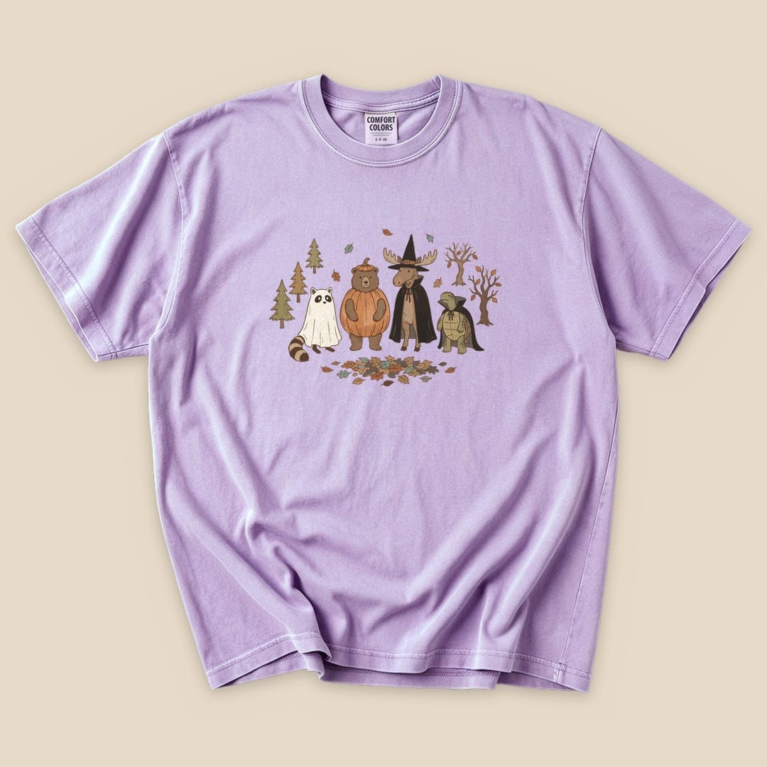 Graphic t-shirt features a whimsical design of animals in costumes, titled "Forest Friends Costume Party T-Shirt," set against a lavender background.