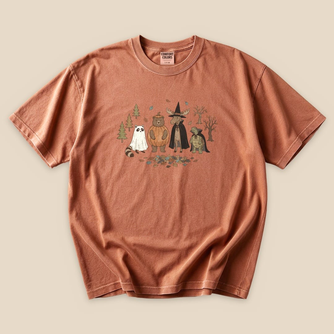 The Forest Friends Costume Party T-Shirt features a whimsical graphic of forest animals dressed in costumes, set against a rustic background.