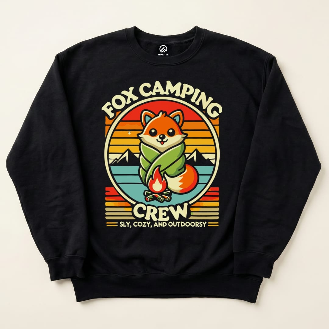 A graphic sweatshirt featuring a cute fox wrapped in a blanket with the words "Fox Camping Crew" and a campfire design.