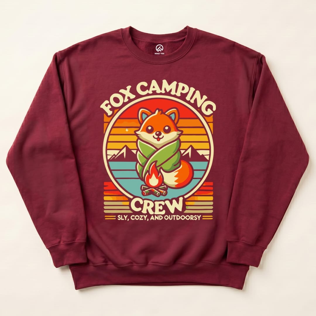 A burgundy graphic sweatshirt features a cartoon fox wrapped in a blanket by a campfire, with "Fox Camping Crew" printed above.