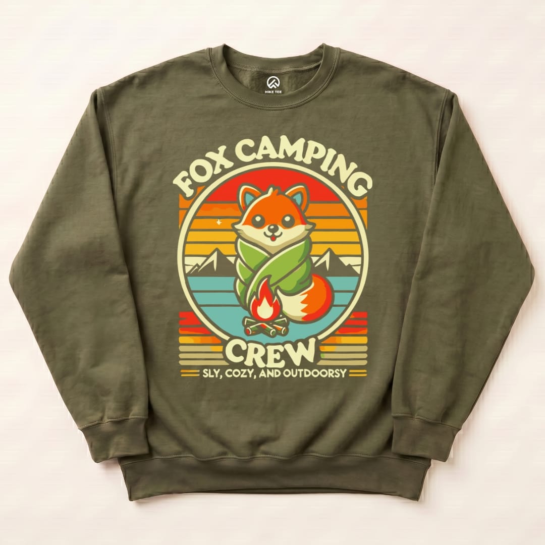 A flat lay of the Fox Camping Crew Sweatshirt features a playful fox wrapped in leaves, sitting by a campfire with mountains in the background.