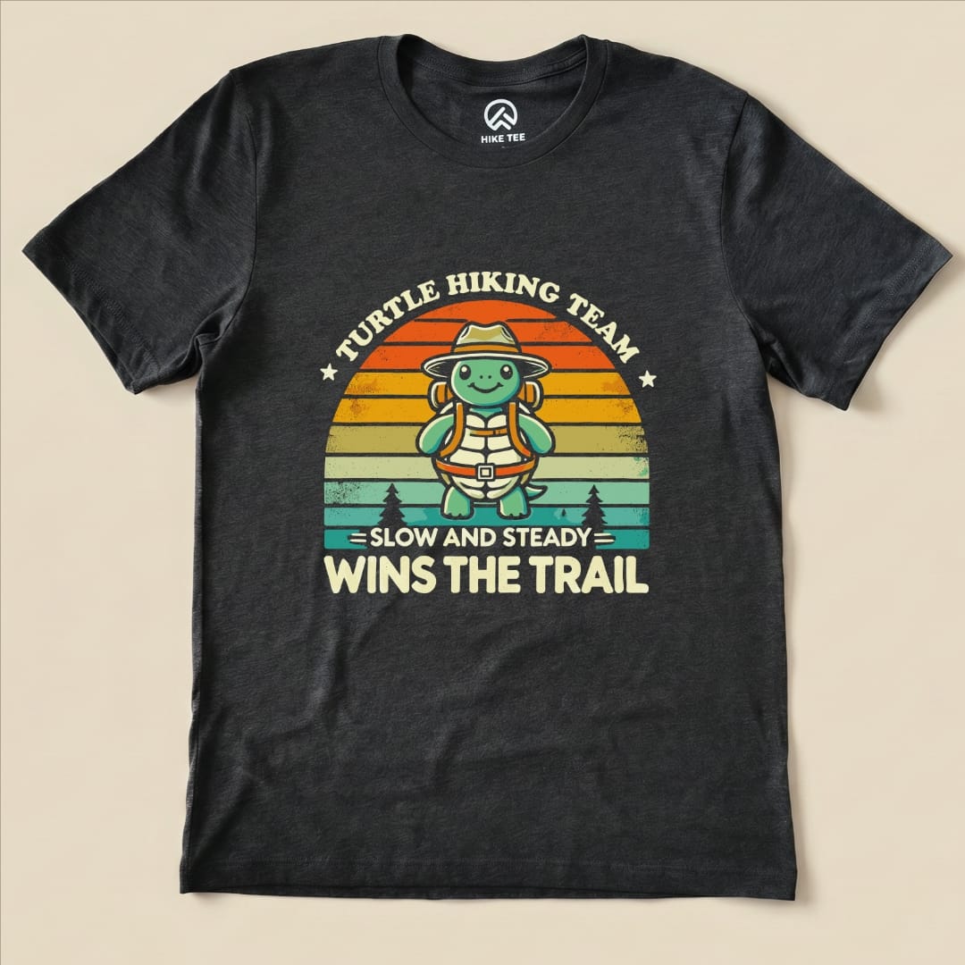 A graphic t-shirt featuring a cartoon turtle in hiking gear, with the text "Turtle Hiking Team - Slow and Steady Wins The Trail".