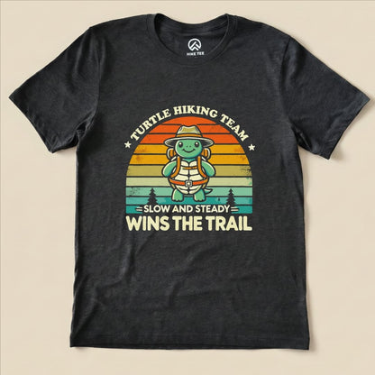 A graphic t-shirt featuring a cartoon turtle in hiking gear, with the text "Turtle Hiking Team - Slow and Steady Wins The Trail".