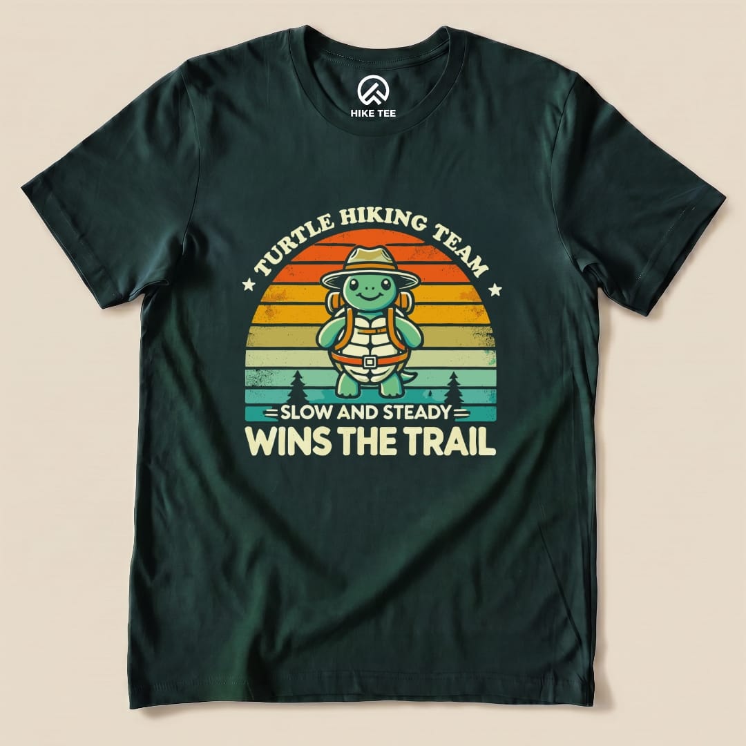 A graphic t-shirt featuring a cheerful turtle in a hat and backpack, with the slogan "Slow and Steady Wins the Trail" and "Turtle Hiking Team.