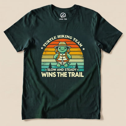 A graphic t-shirt featuring a cheerful turtle in a hat and backpack, with the slogan "Slow and Steady Wins the Trail" and "Turtle Hiking Team.