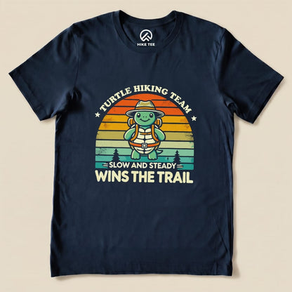 The Funny Turtle Hiking Team Shirt features a cheerful turtle in a hat and backpack with the slogan "Slow and Steady Wins the Trail" printed on navy fabric.