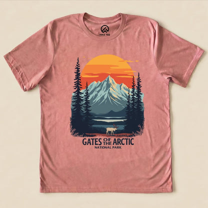 A pink graphic t-shirt featuring a scenic design with mountains, a sunset, and a caribou, labeled "GATES OF THE ARCTIC NATIONAL PARK.