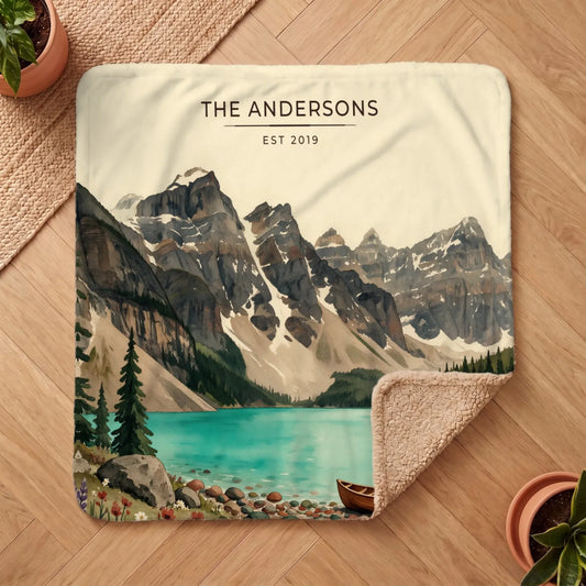 A beautifully illustrated Glacier Lake Canoe Sherpa Blanket features serene mountains and tranquil waters with a canoe by the shore.