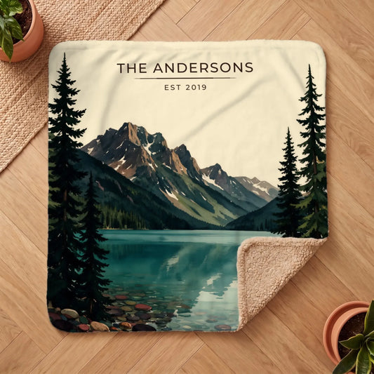 A cozy "Glacier Lake McDonald Sherpa Blanket" features a scenic mountain landscape with evergreen trees and a serene lake.
