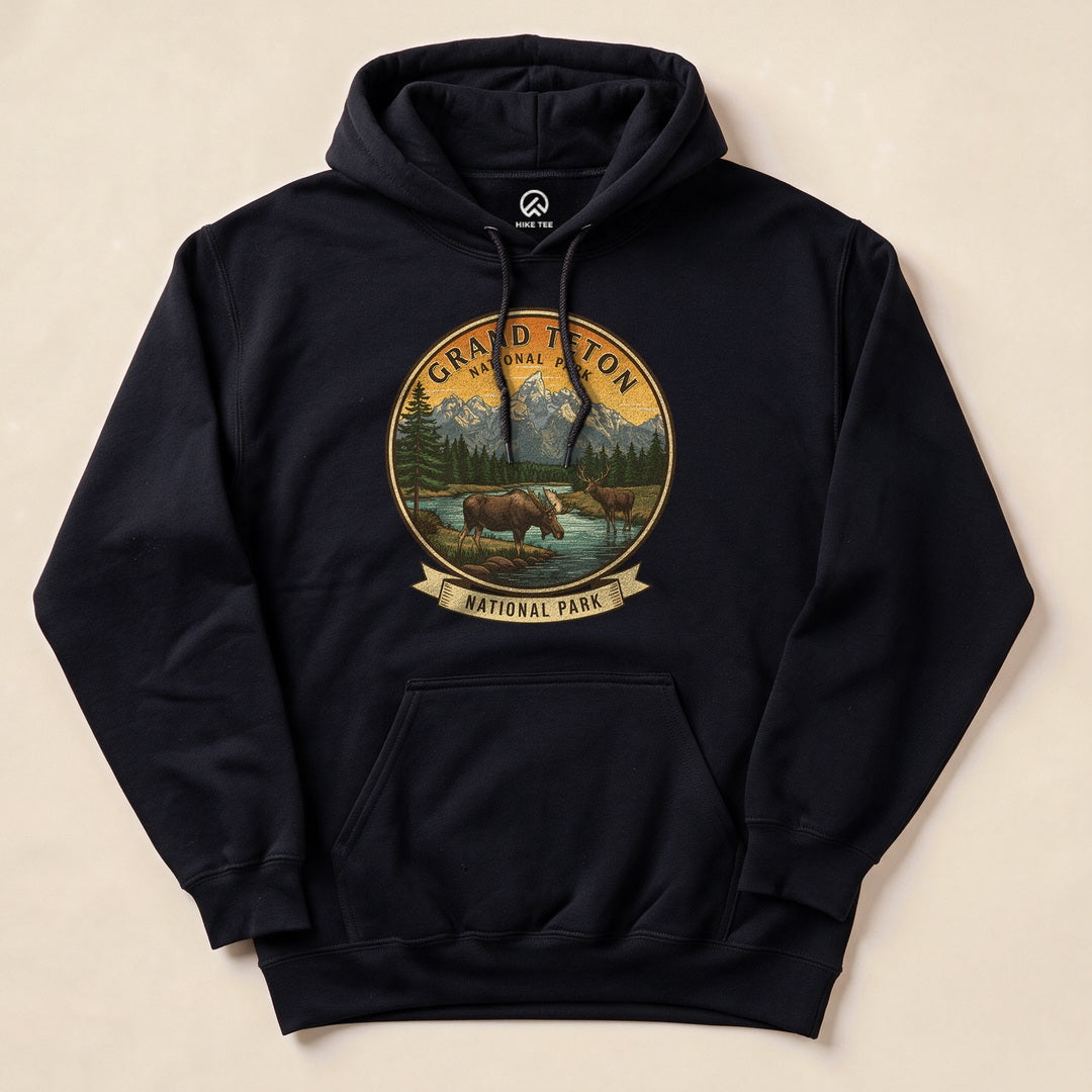 Black hoodie featuring a graphic design of two moose near a river, surrounded by mountains, labeled "Grand Teton National Park.
