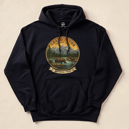Black hoodie featuring a graphic design of two moose near a river, surrounded by mountains, labeled "Grand Teton National Park.