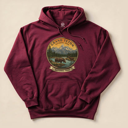 A maroon Grand Teton Moose Hoodie featuring a graphic of moose by a river with mountains in the background and a circular design.