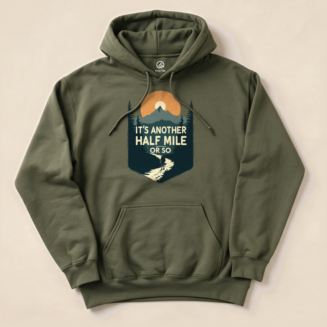 A flat lay of the Half Mile Hoodie in olive green featuring a graphic design with mountains, sun, and the text "It's Another HALF MILE or so.