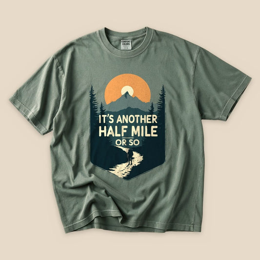 Graphic t-shirt featuring a mountainous sunset design with the phrase "It's another HALF MILE or so" prominently displayed.