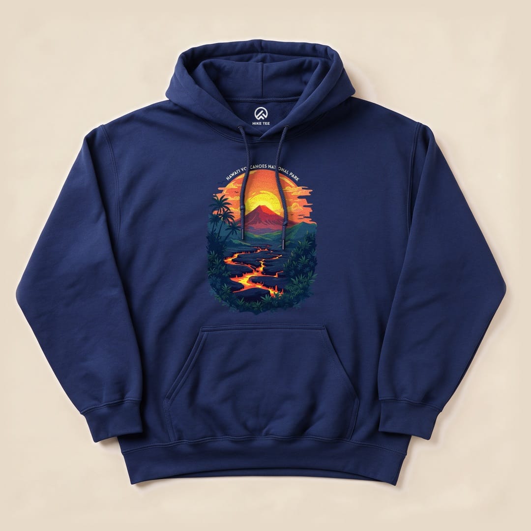 A navy blue hoodie featuring a vibrant graphic of the sun setting over Hawai'i Volcanoes National Park with flowing lava, surrounded by palm trees.