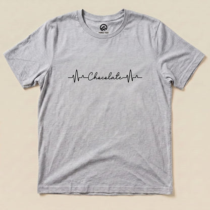 A flat graphic t-shirt featuring a heartbeat line with the word "Chocolate" integrated into the design, labeled as "Heart Beat Chocolate Shirt.