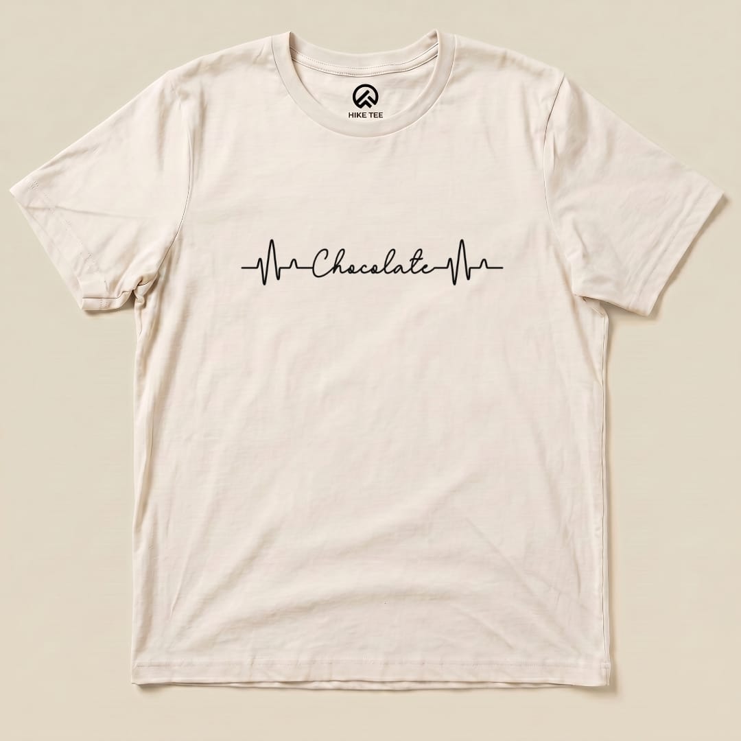 A flat lay of the Heart Beat Chocolate Shirt displaying the word "Chocolate" integrated into a heartbeat line graphic on a cream background.