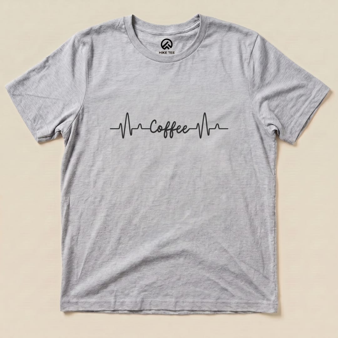 A flat graphic t-shirt in light gray featuring a heartbeat line with the word "Coffee" printed in a stylish font.