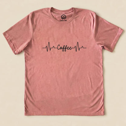A pink graphic t-shirt featuring the slogan "Coffee" with heartbeat lines, labeled as the Heart Beat Coffee Shirt.