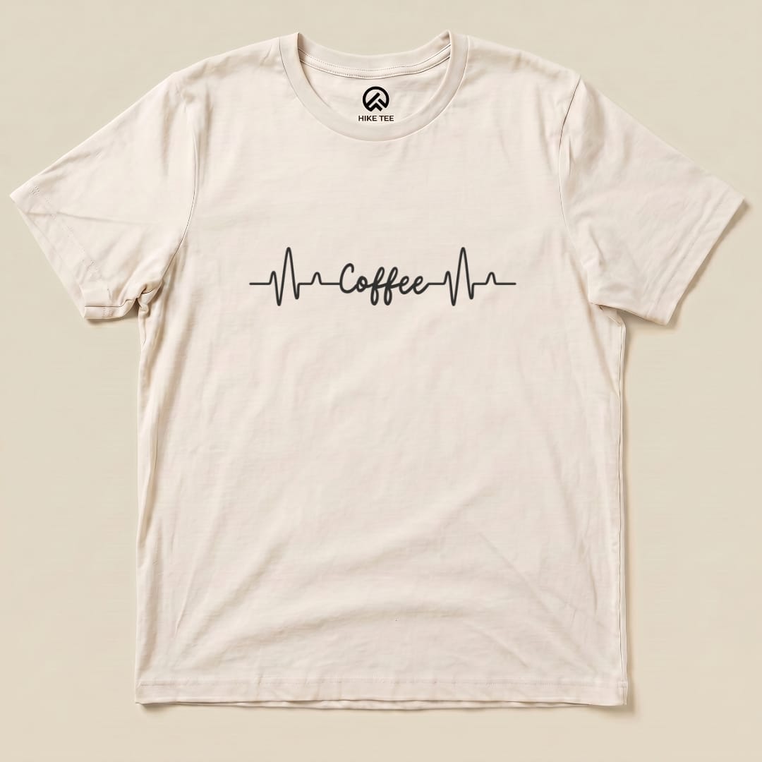A flat graphic t-shirt featuring a heartbeat line design with the word "Coffee" in a playful font, labeled as the Heart Beat Coffee Shirt.