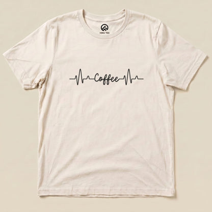 A flat graphic t-shirt featuring a heartbeat line design with the word "Coffee" in a playful font, labeled as the Heart Beat Coffee Shirt.