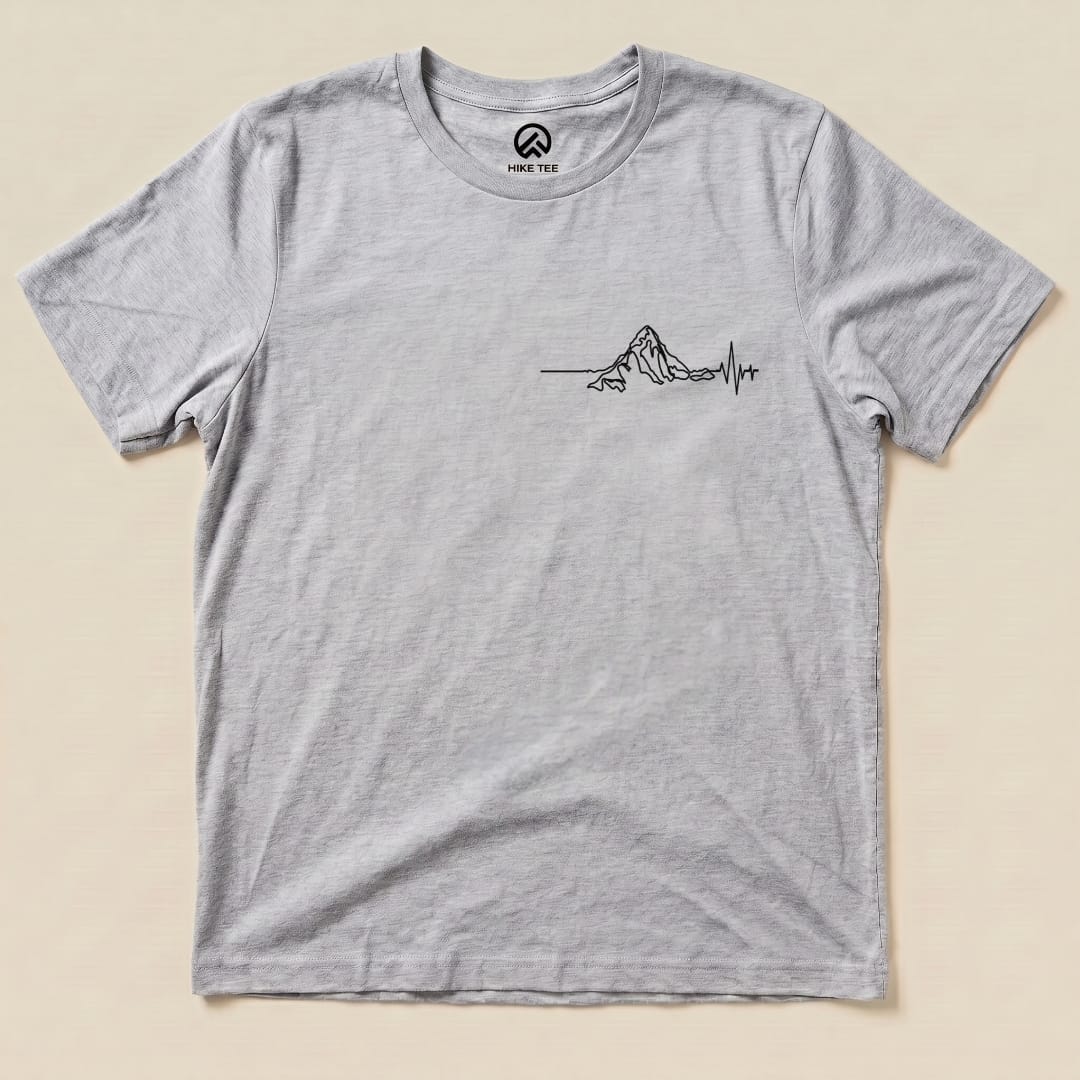 A light gray graphic t-shirt featuring a line art design of a mountain with a heartbeat line, labeled as the "Heart Rate Mountain Shirt.