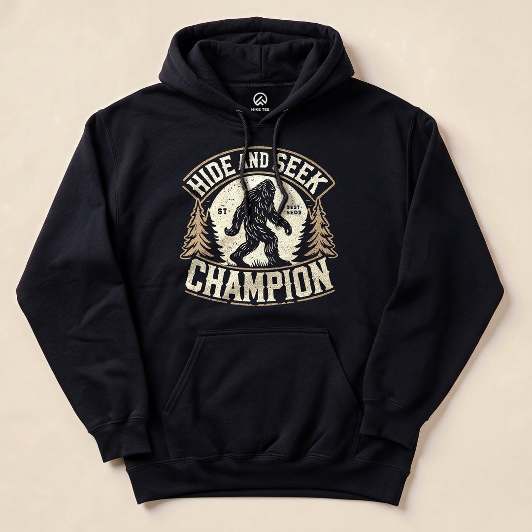 The image features a "Hide and Seek Champion Bigfoot Hoodie" in black, showcasing a graphic of Bigfoot among trees with the slogan “Hide and Seek Champion.”