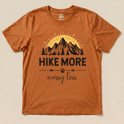 A flat view of the "Hike More Worry Less Shirt" in a burnt orange color featuring a mountain scene and slogan in bold lettering.