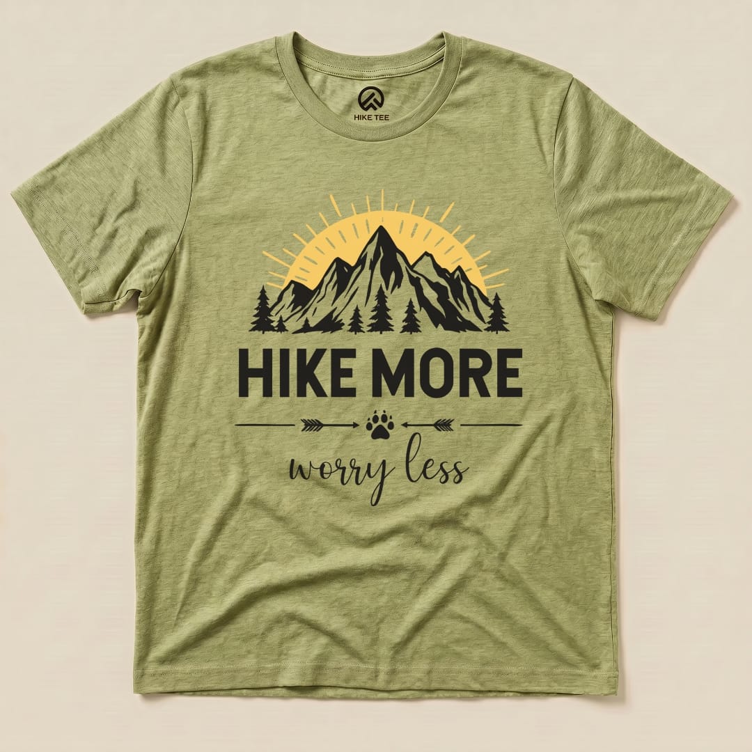 A flat graphic t-shirt in olive green features a mountain scene with the phrase "Hike More Worry Less" prominently displayed.