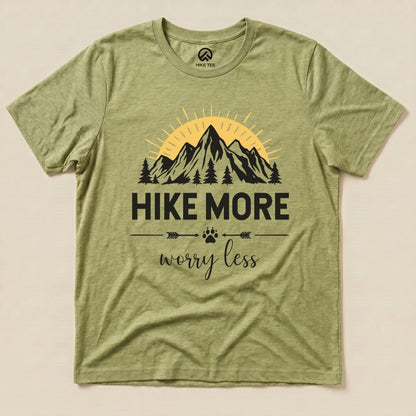 A flat graphic t-shirt in olive green features a mountain scene with the phrase "Hike More Worry Less" prominently displayed.