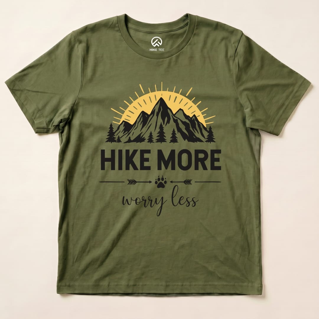 The Hike More Worry Less Shirt features a graphic of mountains, a sun, and trees, with the slogan prominently displayed in black print.