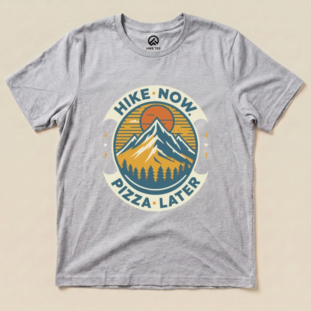 Gray graphic t-shirt featuring mountains and the slogan "Hike Now Pizza Later," perfect for outdoor enthusiasts.