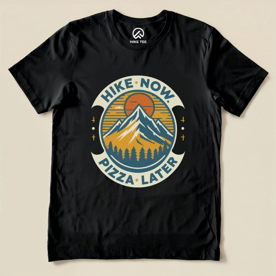 Graphic t-shirt featuring the slogan "Hike Now Pizza Later" with mountains and trees, perfect for outdoor enthusiasts.