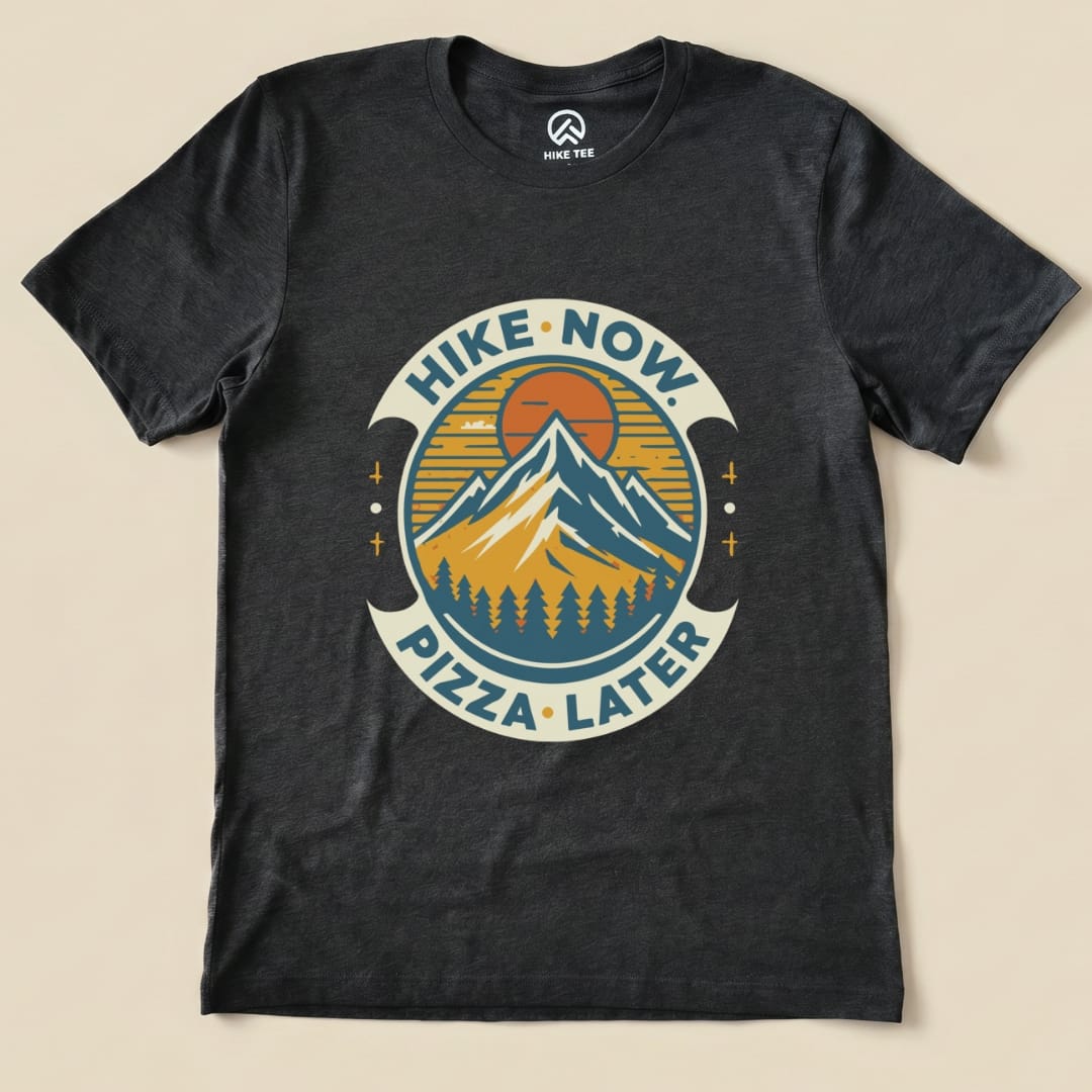 Graphic t-shirt featuring mountains, a sun, and the slogan "Hike Now Pizza Later Shirt - del" in a circular design.